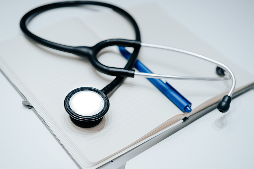 Stethoscope lying on top of an open notebook and pen