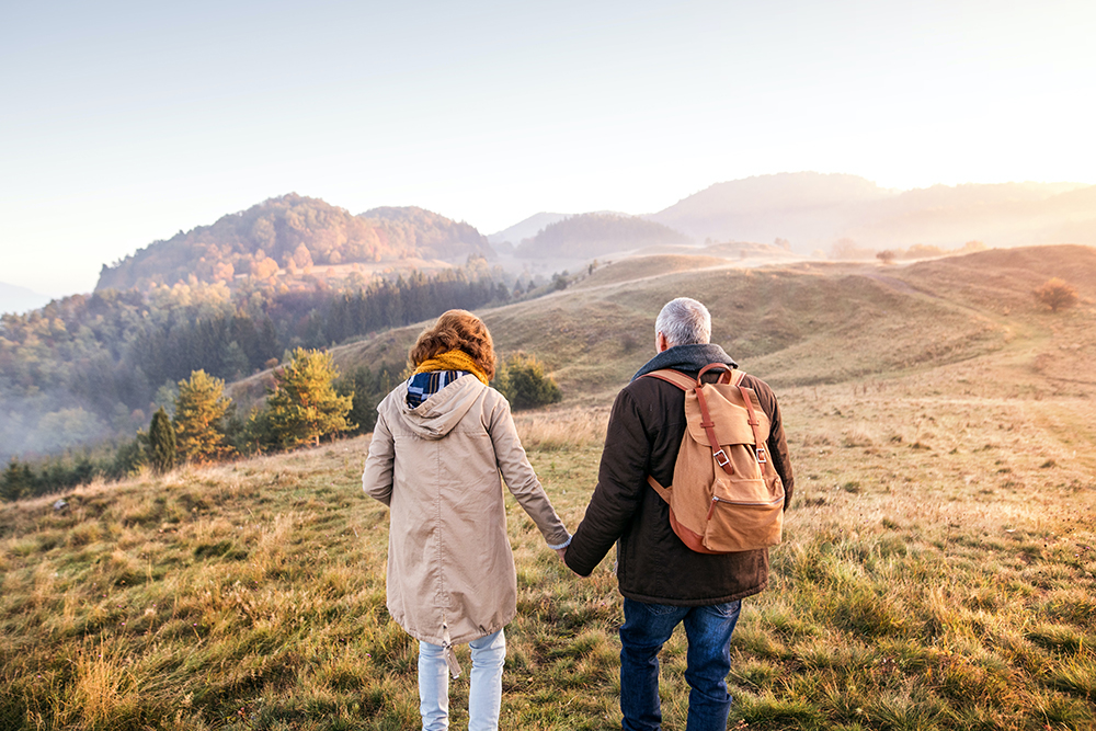 Older couple holding hands walking away from camera on a hilltop in the countryside