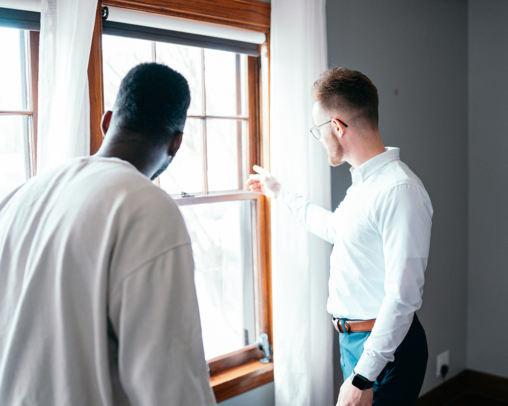 Two men in a property with their backs to the camera, looking out the window, viewing it, with one pointing out the window