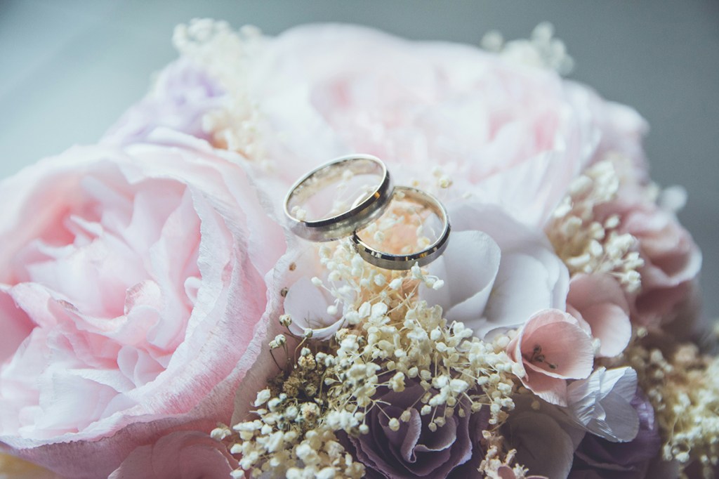 A bouquet of flowers including pink roses with two wedding rings laid on top