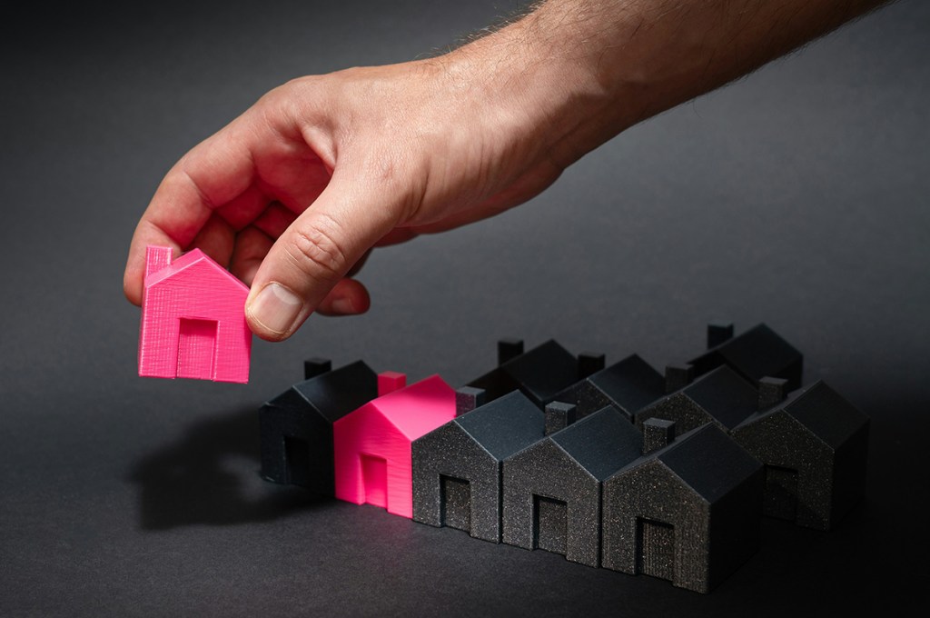 Set of model homes lined up in black, with two homes in red. One of the red homes is being picked up by an arm at the top of the image