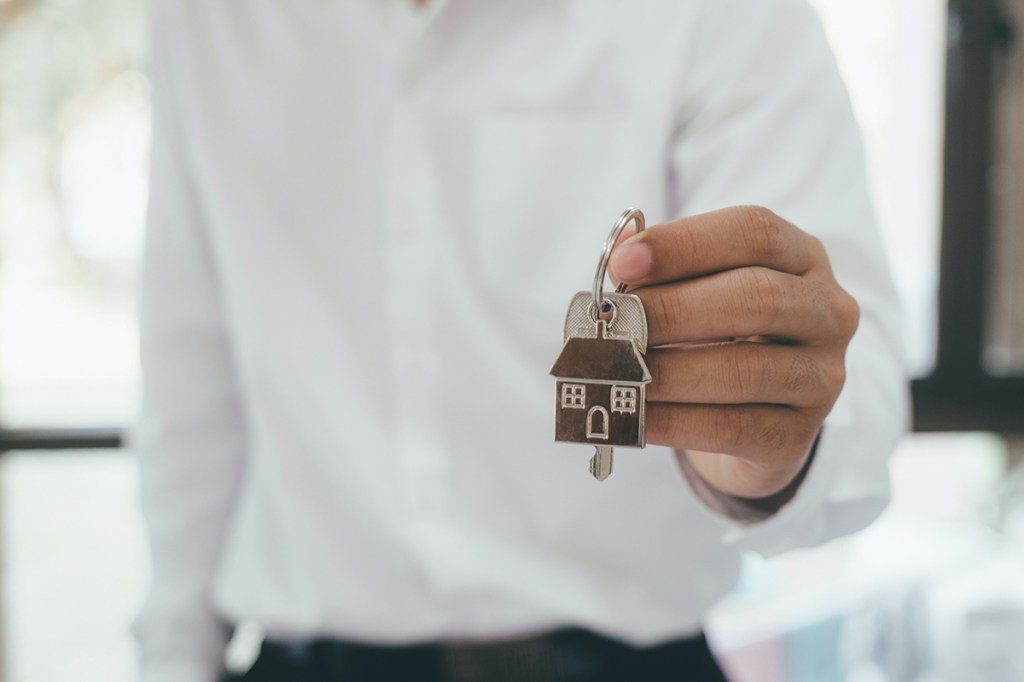 A man in a white shirt holds a keyring towards the camera with a single key and a house tag on it