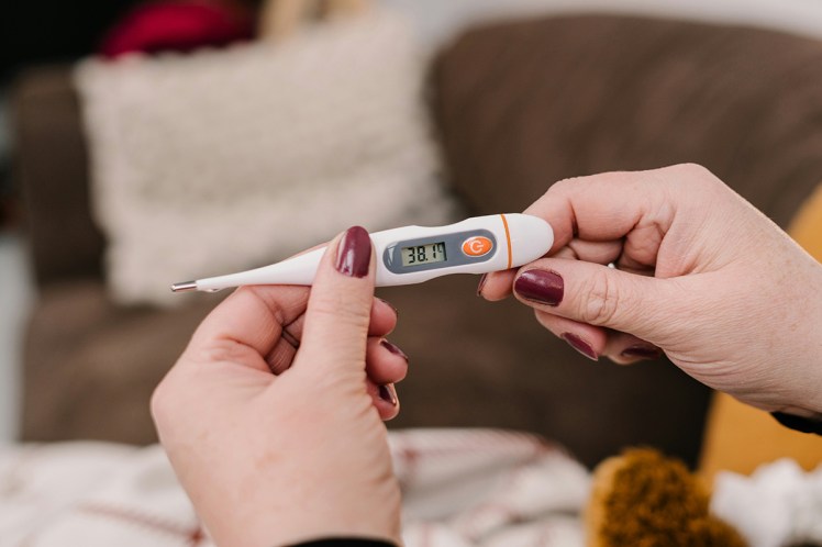 Hands with red-purple nail varnish holding a thermometer showing the temperature as 38.1 degrees
